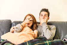 couple sitting on couch looking scared